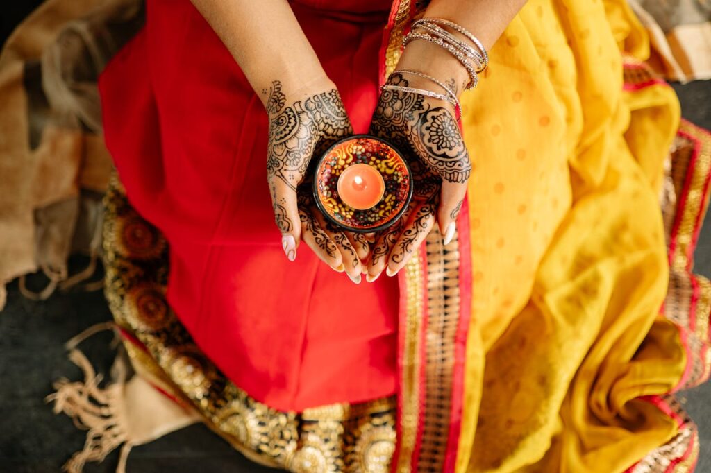pexels photo 8819765 A woman in traditional attire holds a candle, symbolizing light and festivity during Diwali with intricate henna designs on her hands.